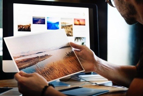 A man reviewing a printed photo while comparing it to a computer screen